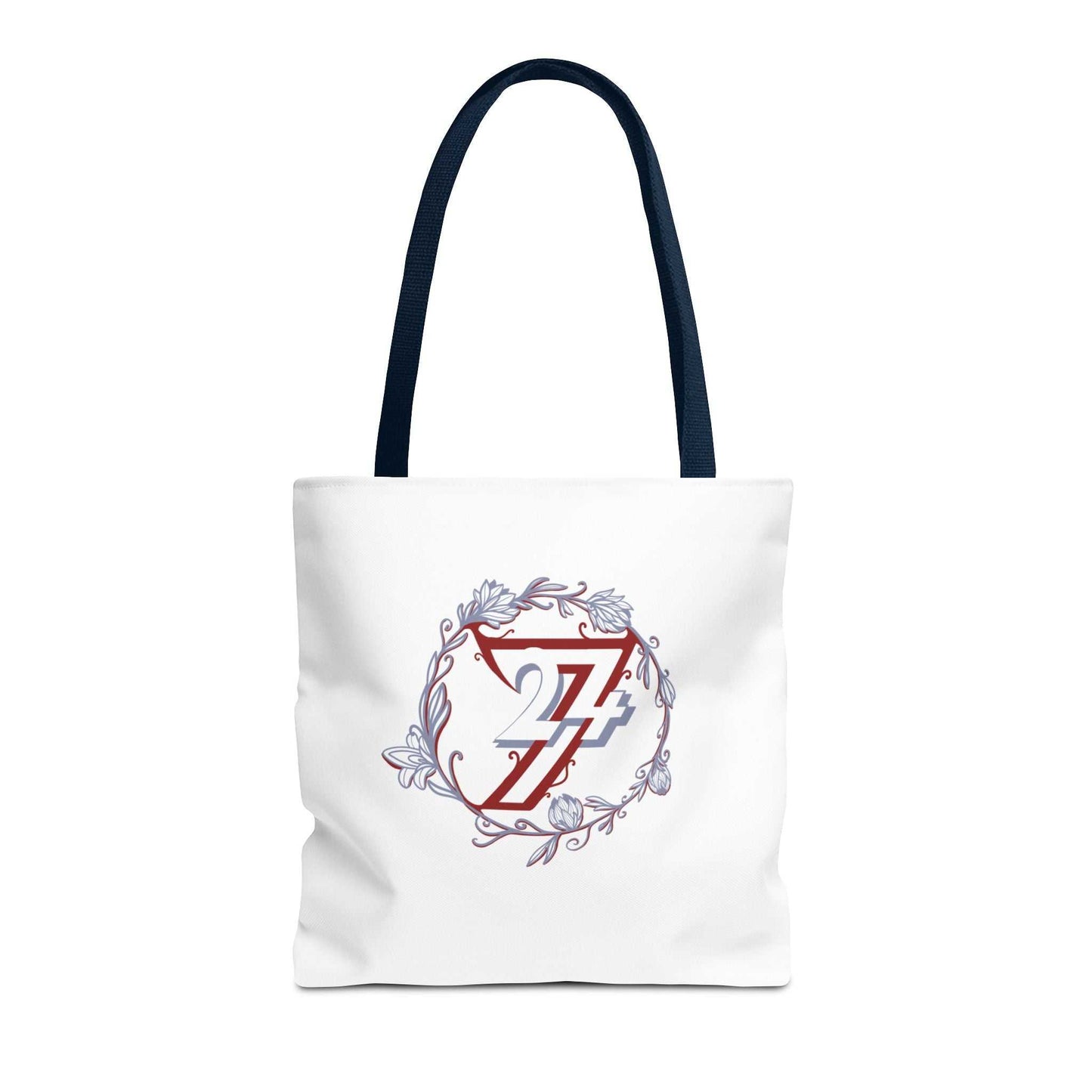 A white canvas tote bag with dark navy blue shoulder straps, featuring a central graphic of a red and blue 24/7 monogram inside a circular floral wreath with light blue accents.