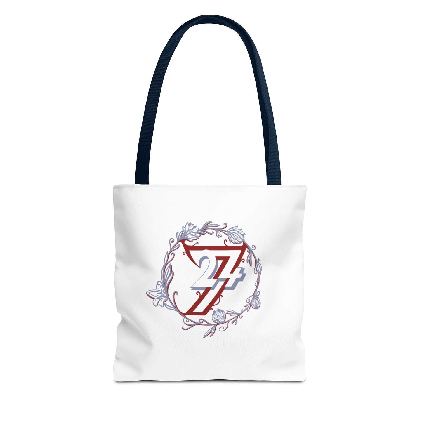 A white canvas tote bag with dark navy blue shoulder straps, featuring a central graphic of a red stylized 24/7 logo inside a circular frame with light blue and gray floral elements.