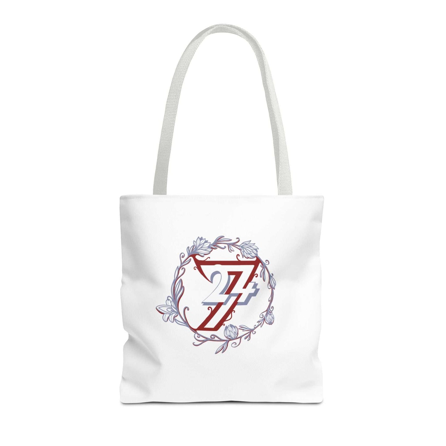 A white canvas tote bag with white shoulder straps, featuring a central graphic of a red stylized 24/7 monogram inside a circular floral wreath with light blue accents.