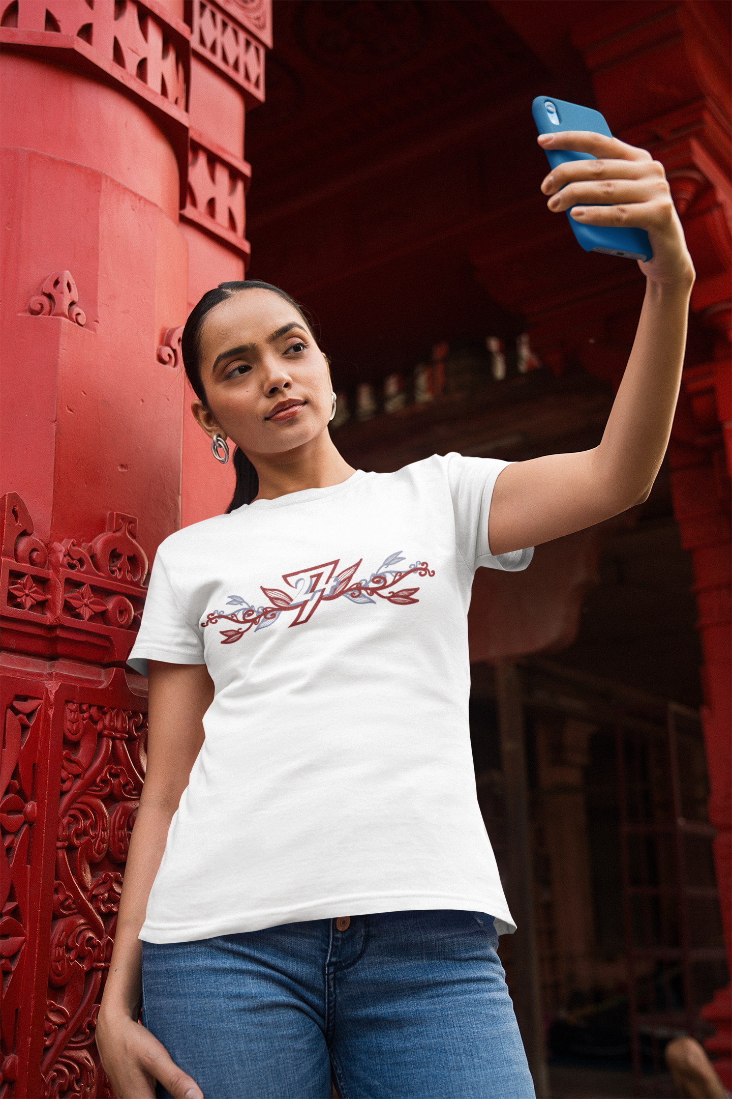 Woman wearing a semi-fitted white women's tshirt featuring the elegant maroon and blue botanical 24/7 logo graphic.