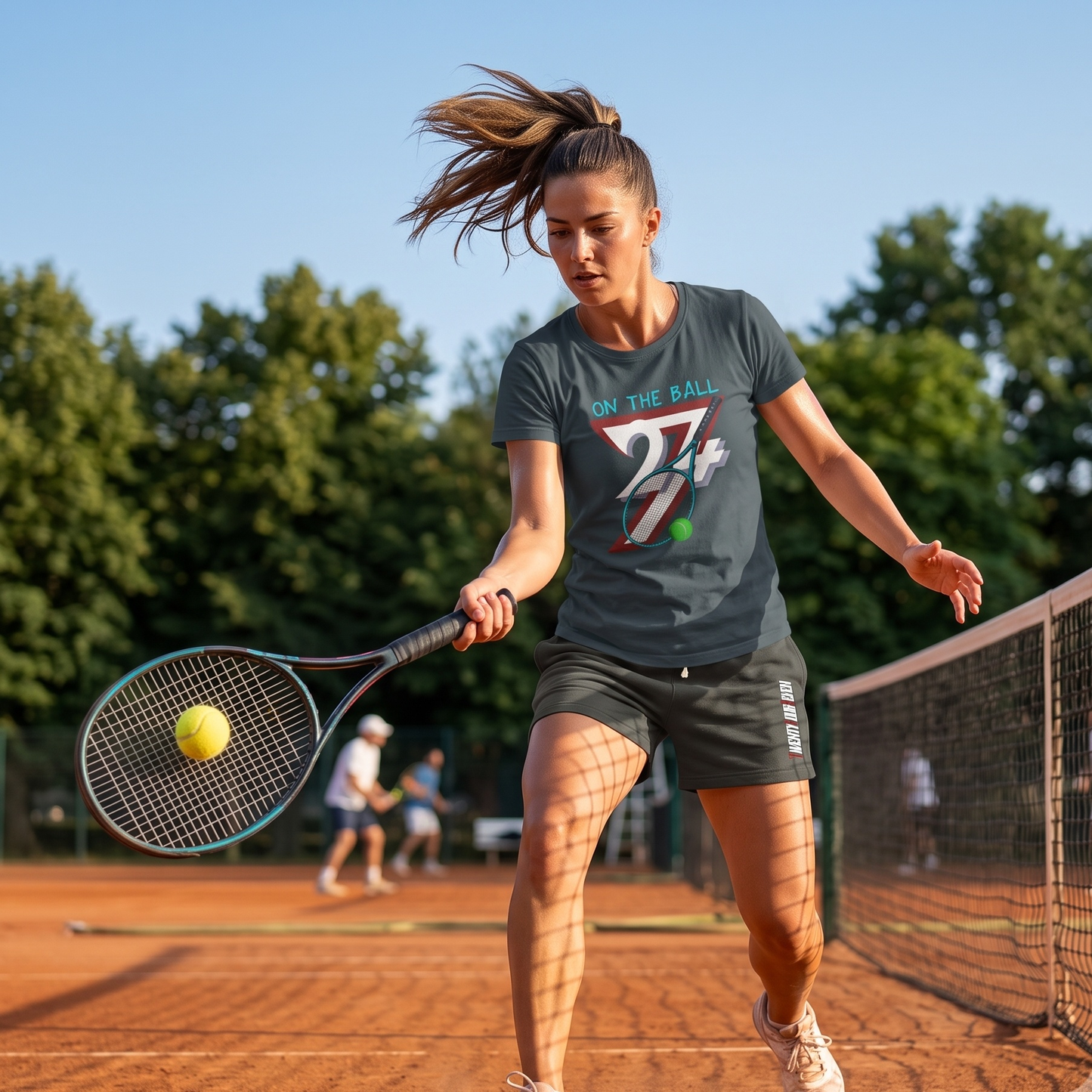Athletic woman lunging for a forehand shot on a red clay tennis court wearing the dark heather grey vintage tennis graphic tee, highlighting its relaxed fit in motion.