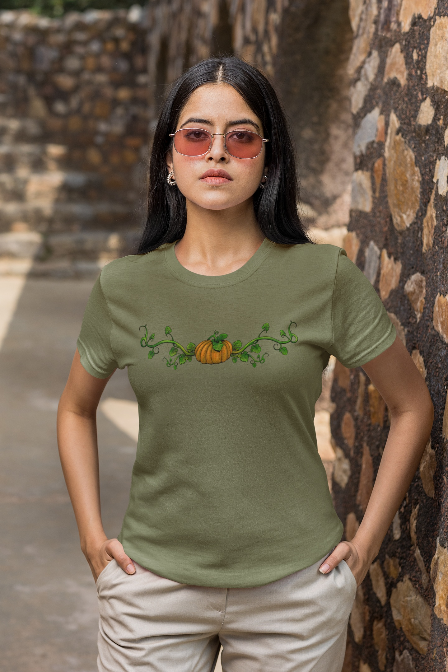 Woman wearing a green t-shirt with a pumpkin design in front of a stone wall.